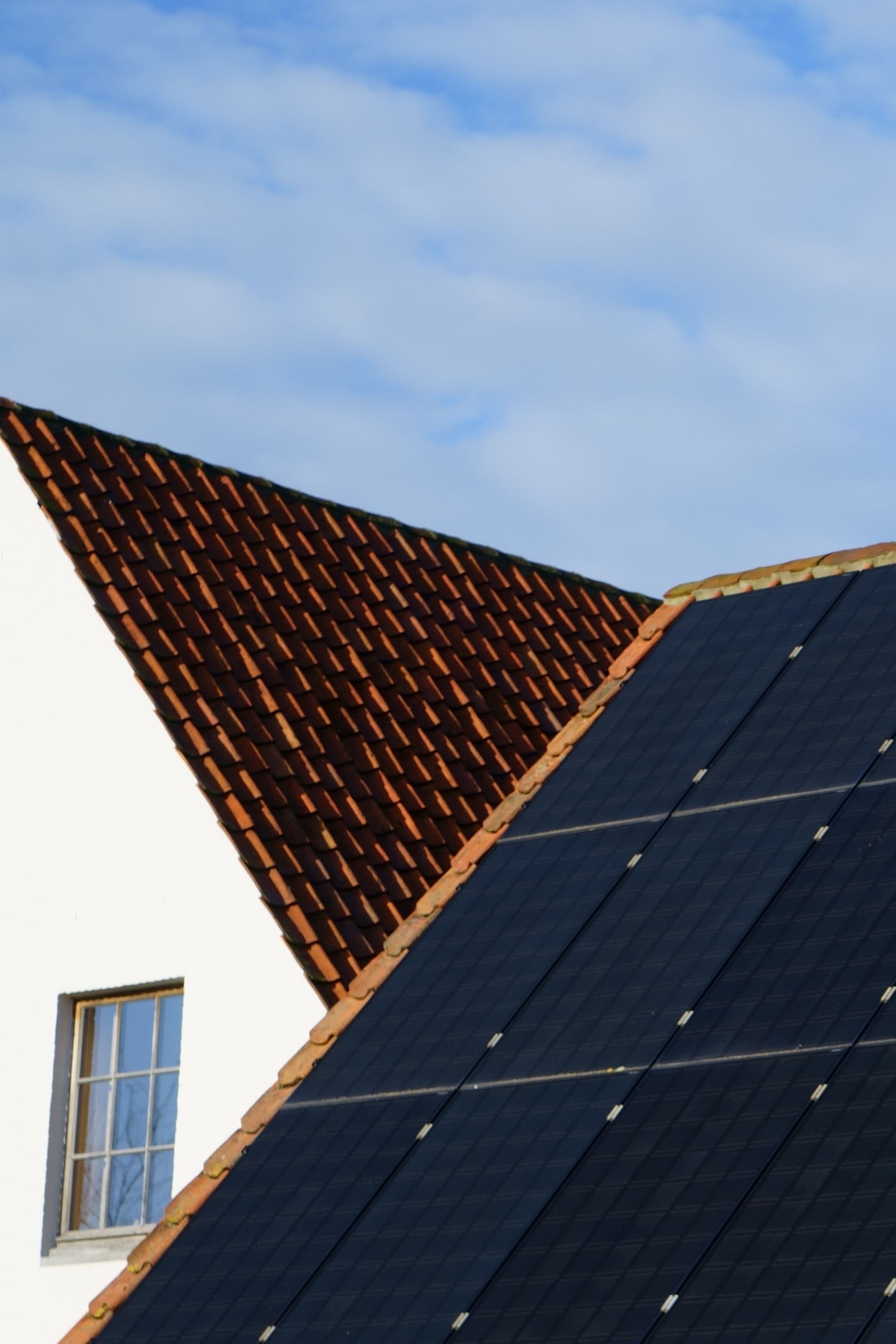 Black solar panels on a tiled roof under a blue sky